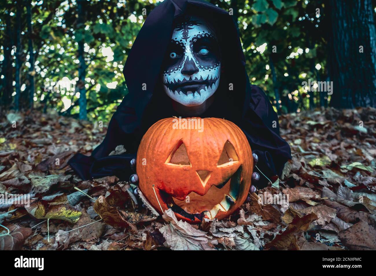 Young woman with halloween paint face mask wearing black hood Scary