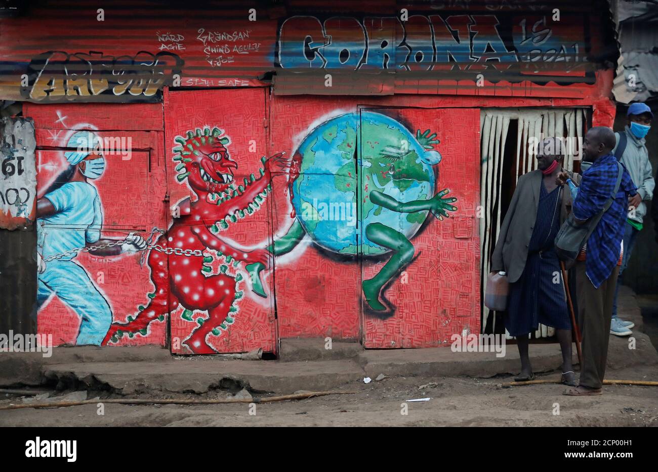 Vendors carrying traditional medicine in jerrycans, stand outside a stall which has graffiti against the spread of the coronavirus disease (COVID-19) within Kibera slums in Nairobi, Kenya July 6, 2020. REUTERS/Thomas Mukoya Stock Photo