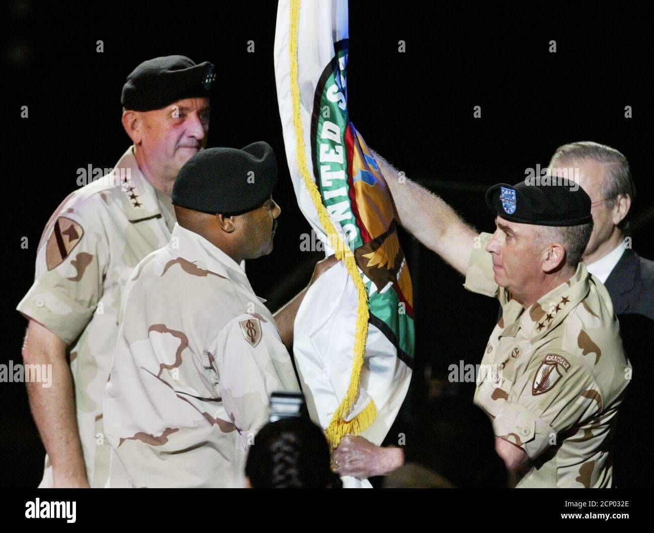 U.S. Army General Tommy Franks (L) looks on as the U.S. Central Command flag is passed to Command Sgt. Major Dwight Brown, (second from left) by Army Gen. John Abizaid who replaces Franks during a change of command ceremony in Tampa, Florida July 7, 2003. Obscured at right is Secretary of Defense Donald Rumsfeld. The U.S. Central Command is headquartered at MacDill Air Force Base in Tampa. REUTERS/Pierre DuCharme Stock Photo