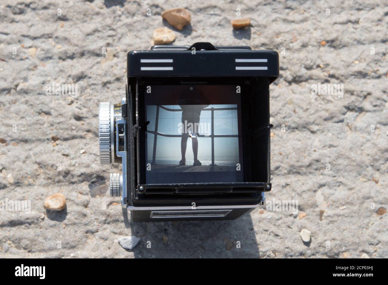 A vintage Rolleiflex twin reflex camera framing a subject in a beach scene in the viewfinder Stock Photo