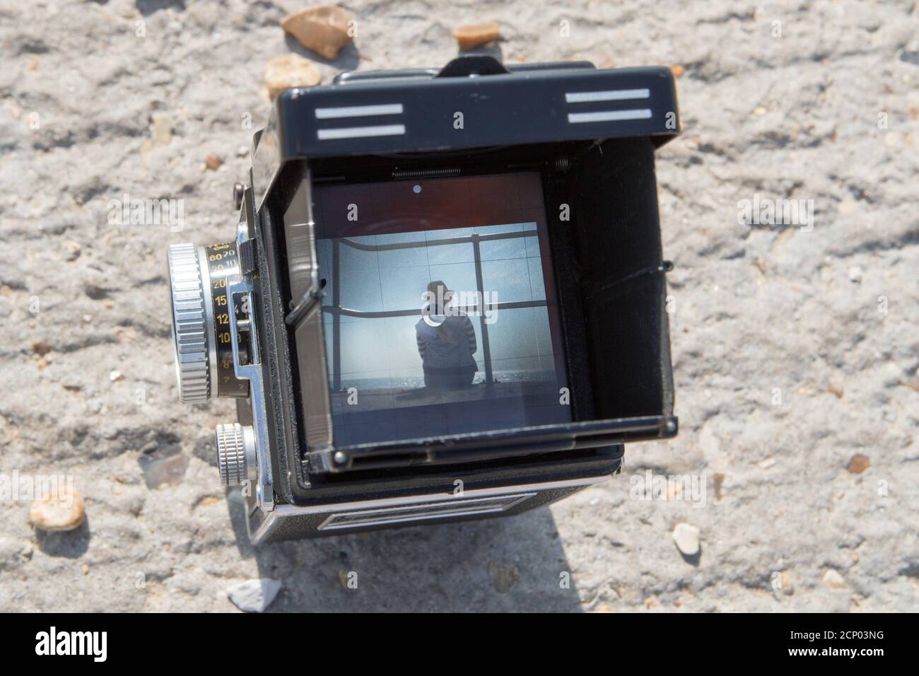 A vintage Rolleiflex twin reflex camera framing a subject in a beach scene in the viewfinder Stock Photo