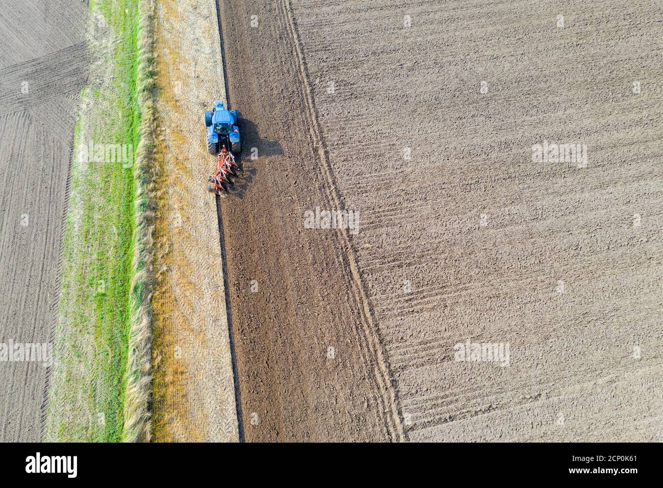 An aerial view of a tractor plowing a barren field for future crops. Stock Photo