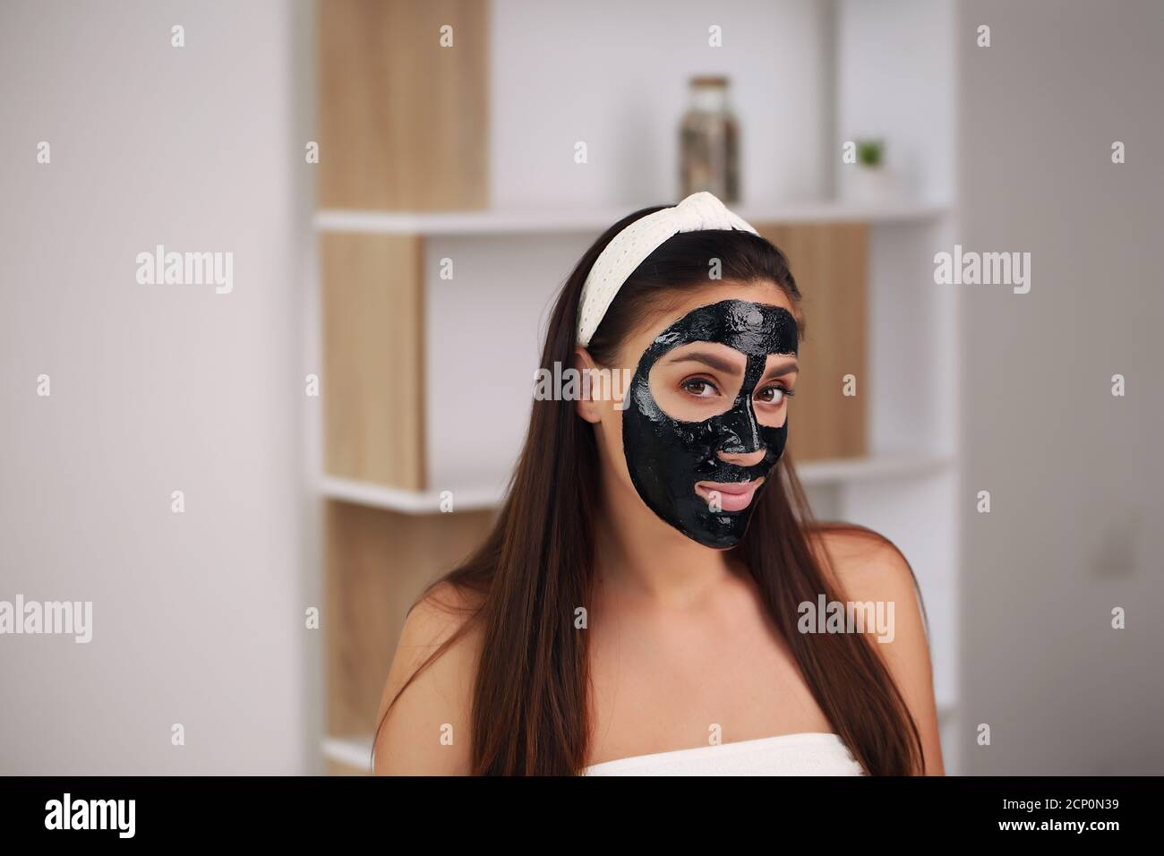 Young woman with carbon detox black mask on face, teenage girl takes care of oily skin, cleansing pores. Beauty salon. Skin care. Stock Photo