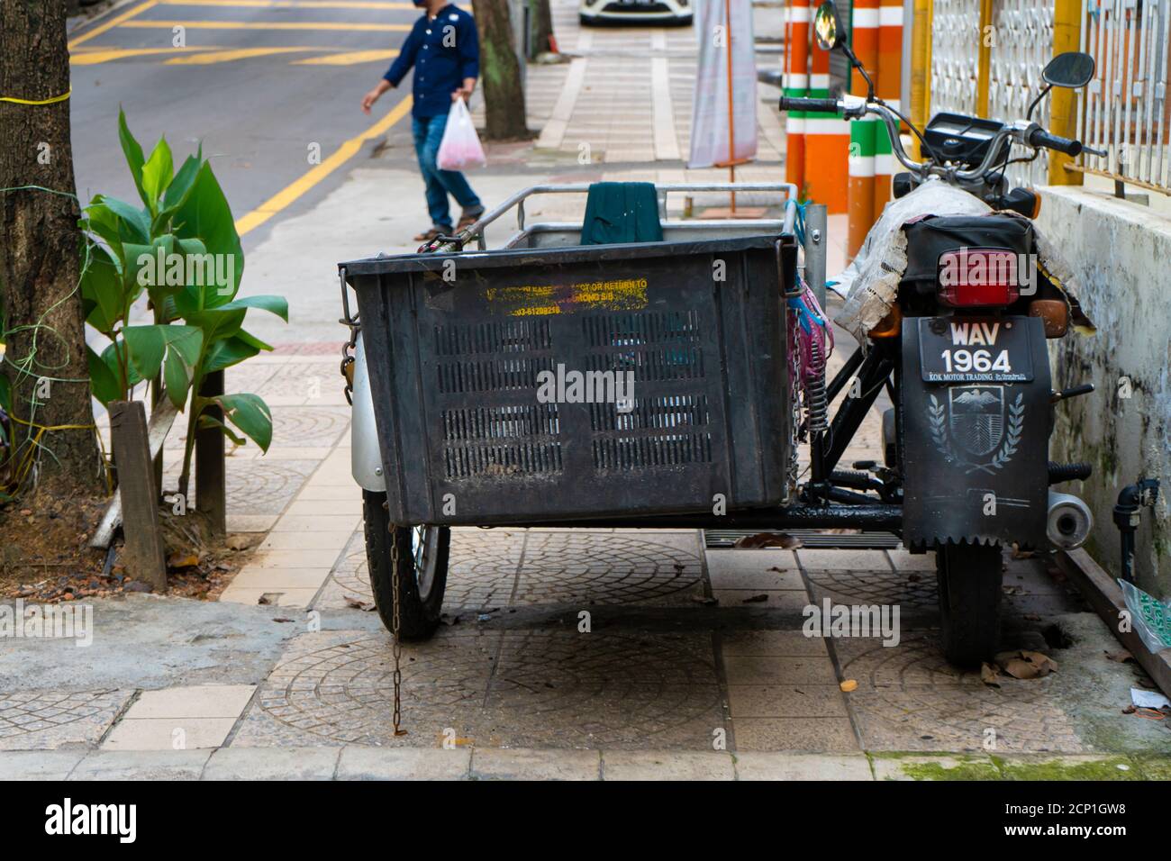 A motorcycle with a sidecar for transporting products blocks the passage along the pedestrian sidewalk. Street trading in Asia. Stock Photo