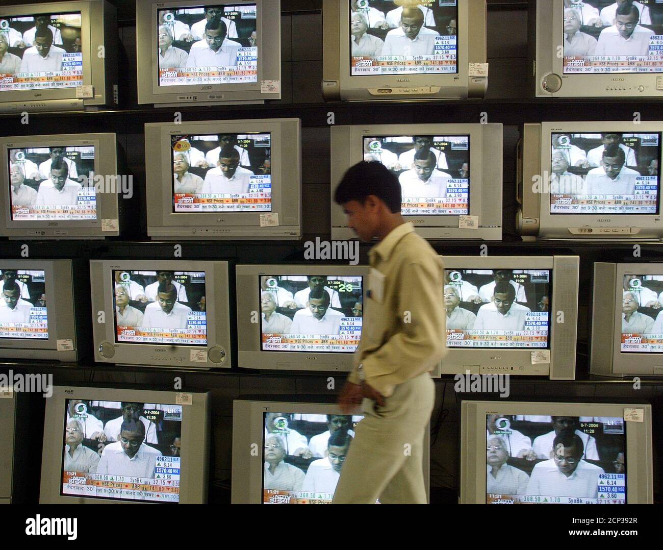 A salesman at an electronic goods shop walks past television sets showing the speech of Indian Finance Minister Palanippan Chidambaram, as he presents the budget in parliament for the fiscal year 2004-05 in Bombay, July 8, 2004. Chidambaram called for sustaining economic growth of 7-8 percent in Asia's third-largest economy when unveiling the budget.REUTERS/Arko Datta  AD/TW Stock Photo