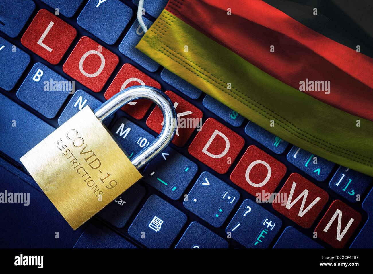 Germany COVID-19 coronavirus lockdown restrictions concept illustrated by padlock on laptop red alert keyboard buttons and face mask with German flag. Stock Photo