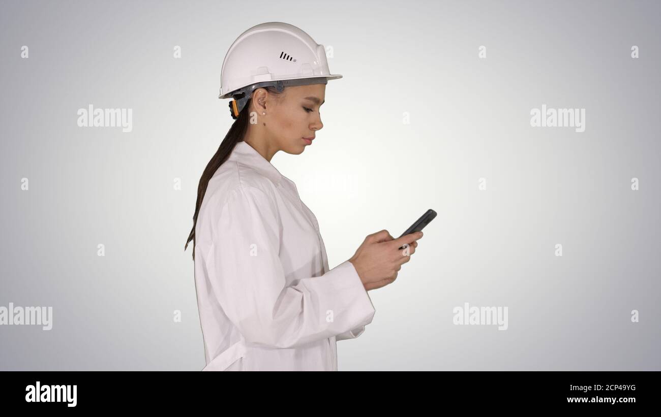 Engineer using mobile phone texting while walking on gradient ba Stock Photo