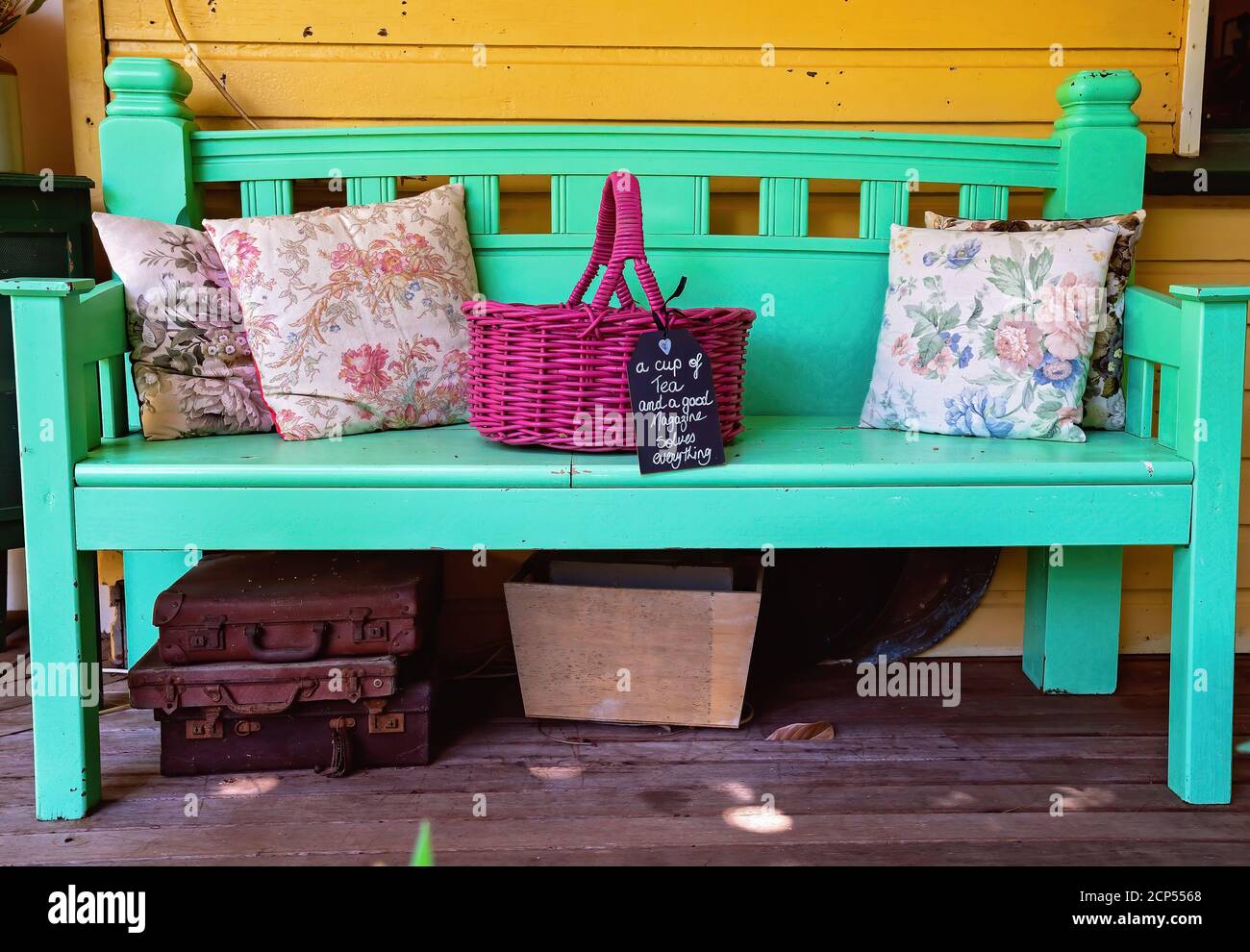 A painted timber bench stacked with cushions and a basket with briefcases and a box underneath including a cute handwritten sign all old fashioned Stock Photo