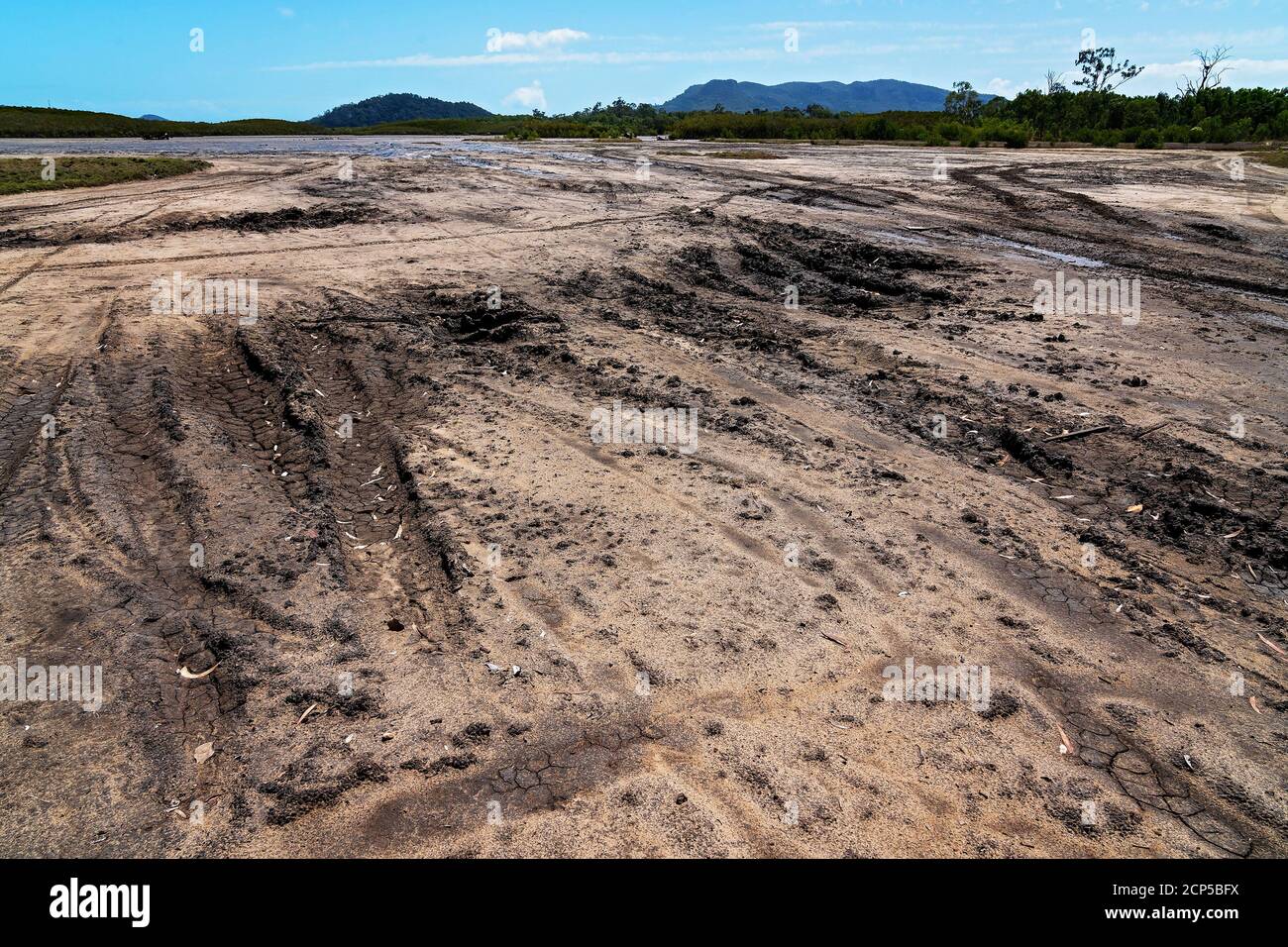 Vehicle tracks gouge out the mud leading onto a tidal salt pan and a rusting car wreck Stock Photo