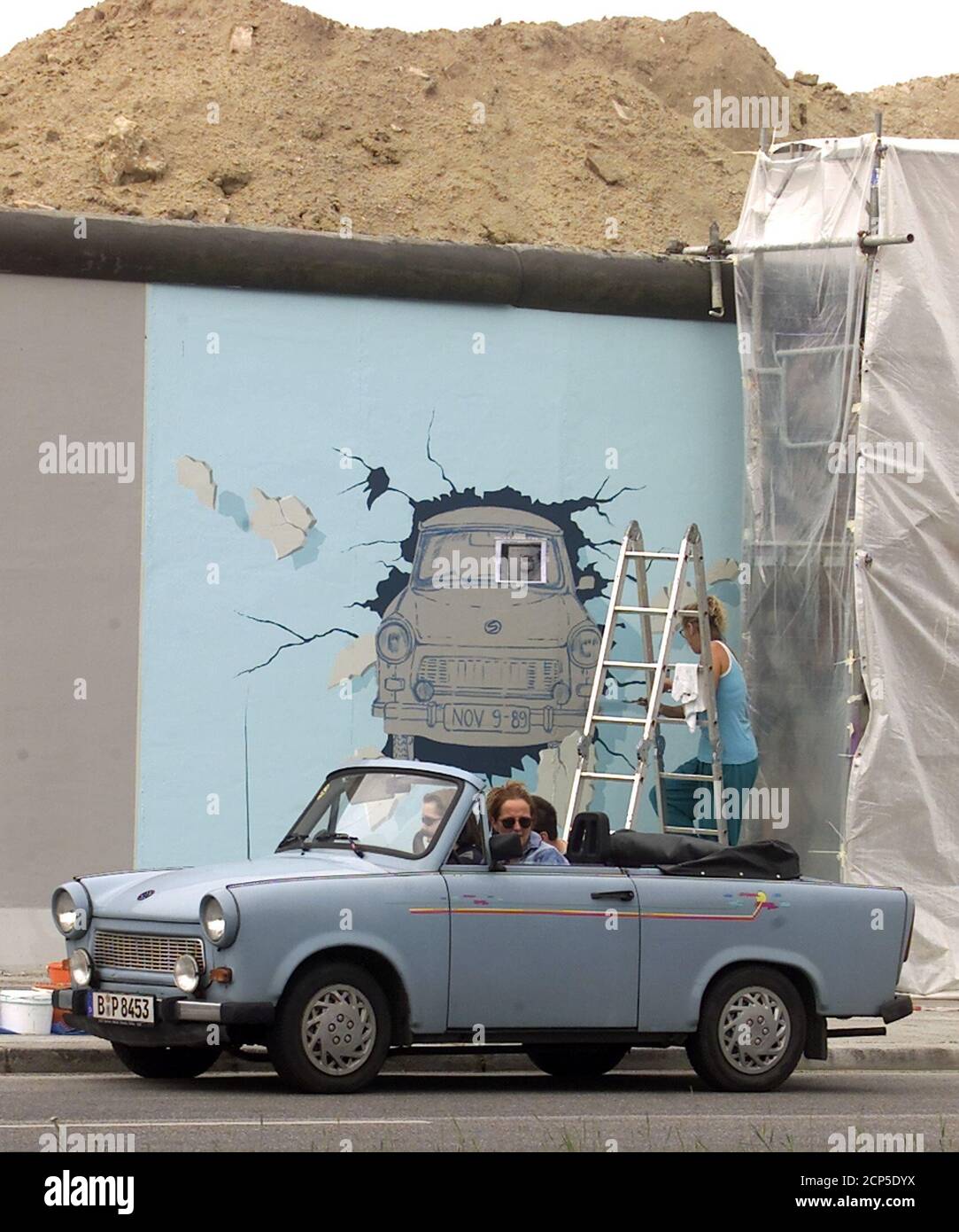 German artist Birgit Kinder (R) repaints a graffiti of the famous east German car Trabant on a segment of the so called East Side Gallery May 26, after the graffiti-painted segments were sandblasted off the largest remaining part of the Berlin Wall, a mile long segment as an original Trabant car stands beside the wall.  FAB/WS Stock Photo