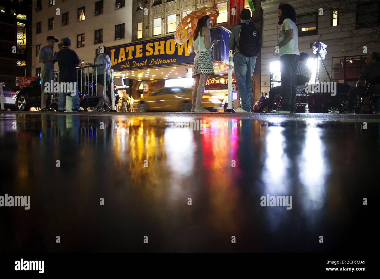 People stand and wait for a sign crew to remove the marquee across the street from the Ed Sullivan Theater where "The Late Show" with David Letterman used to tape in the Manhattan borough New York May 27, 2015. The taping and broadcast of the final edition of "The Late Show" was May 20, and workers are now slowly transforming the theater for the show's new host Stephen Colbert which will premiere on September 8, 2015. REUTERS/Carlo Allegri Stock Photo