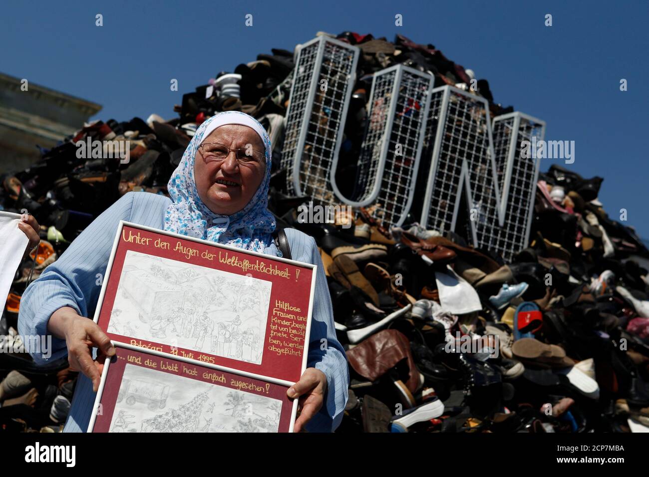 A woman holds drawings during a gathering at the temporary monument 'Pillar of Shame' near the Brandenburg Gate in Berlin, July 11, 2010, commemorating the 1995 mass murder of Muslim men and boys in the town of Srebrenica. The Society for Threatened Peoples has collected 16.744 shoes from Bosnia, Austria, Switzerland and Germany to build the monument that is to draw attention to the failure of the United Nations (UN) to prevent the killing of 8372 refugees who died during the Bosnian War in an area that was declared UN safe zone. The writing reads: 'Under the eyes of the international communit Stock Photo