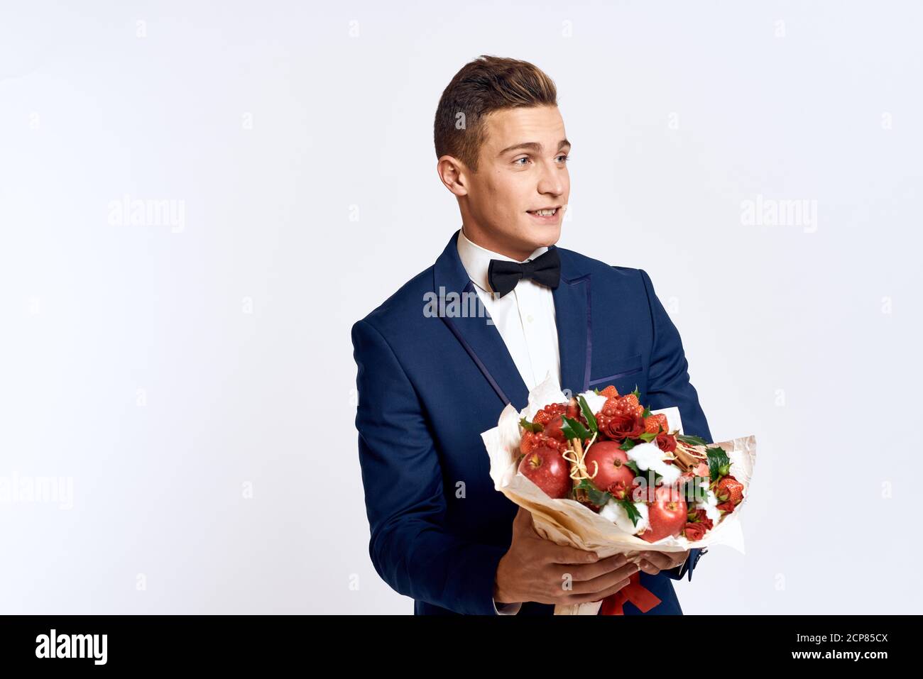 An elegant man in a classic suit with a bow tie holds a bouquet of ...