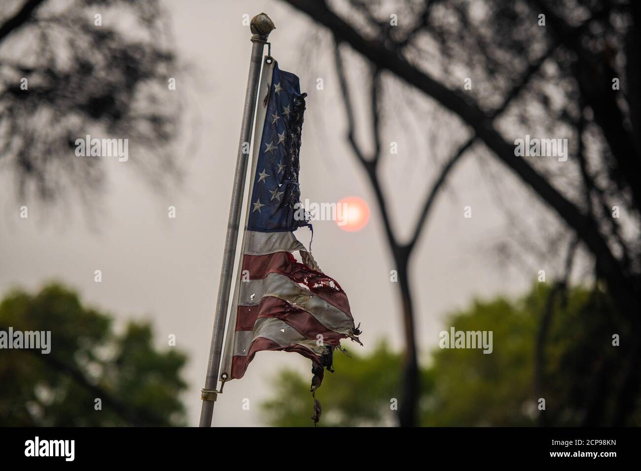 TALENT, ORE - SEPTEMBER 18, 2020: A partially burned American Flag waves with the smoke blocked sun behind it inside Talent Mobile Estates #81 amid the aftermath of the Almeda Fire. The town of Talent, Oregon, showing the burned out homes, cars and rubble left behind. In Talent, about 20 miles north of the California border, homes were charred beyond recognition. Across the western US, at least 87 wildfires are burning, according to the National Interagency Fire Center. They've torched more than 4.7 million acres -- more than six times the area of Rhode Island. Credit: Chris Tuite/imageSPACE/M Stock Photo
