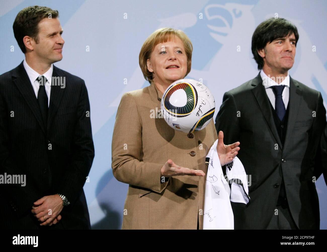 German Chancellor Angela Merkel holds a soccer ball and a jersey with the  signatures of the national squad as she is flanked by national soccer team  manager Oliver Bierhoff and coach Joachim
