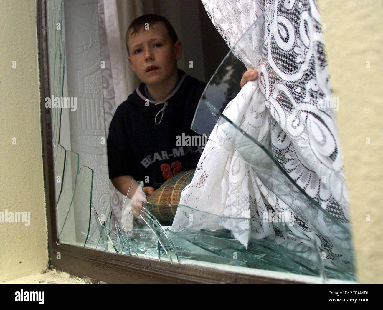A young boy looks out though a smashed front window following trouble with Loyalists attacking nationalists' homes in the Duncain Gardens area of north Belfast, Northern Ireland, June 21, 2002. Trouble flared on the day of the first big march of the contentious Protestant marching season in north Belfast where stones, bricks and other missiles were thrown over the peace line in Duncairn Gardens. REUTERS/Paul McErlane  PM/CRB Stock Photo