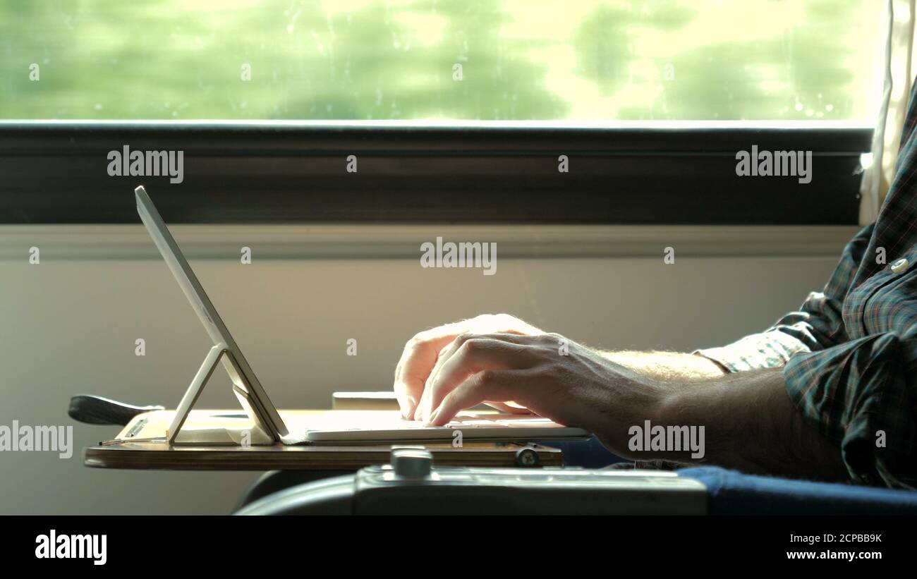 Man hands typing on laptop tablet computer in a train. Stock Photo