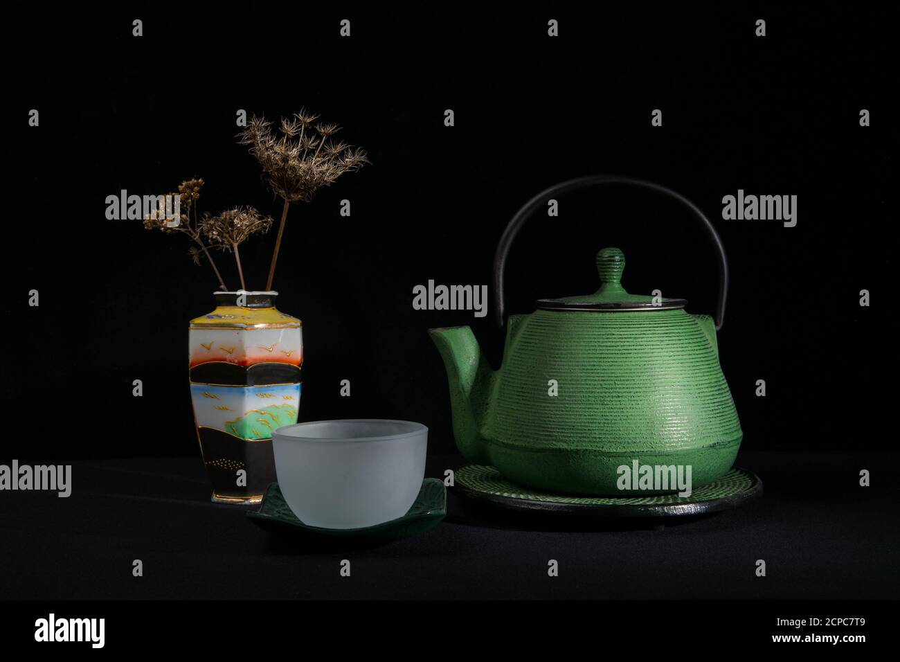 A green metal teapot, a glass bowl and a chinese vase with dried umbels. Isolated on a black background Stock Photo