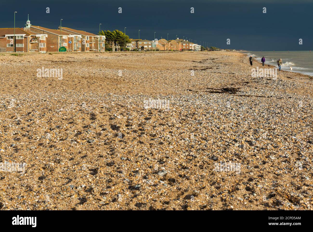 Dark storm clouds approaching the seaside with sunlight lighting up the shingle beach, which is nearly deserted, in England, UK. Stock Photo