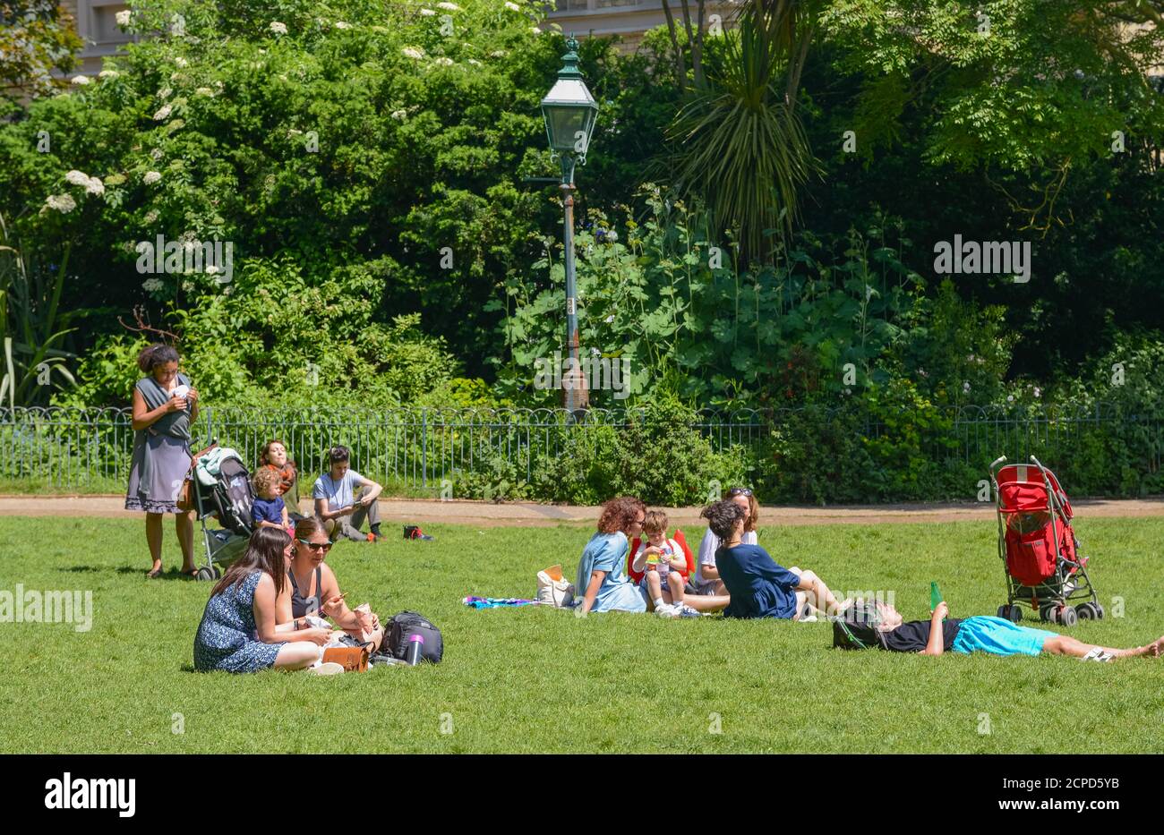 People sitting on grass in the park at The Royal Pavilion Gardens on a hot day in Summer in Brighton, East Sussex, England, UK. Stock Photo