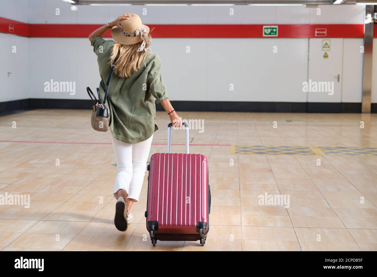 Young woman running because she is loosing the train, she is wearing a hat and carrying a suitcase. Travel concept. Stock Photo