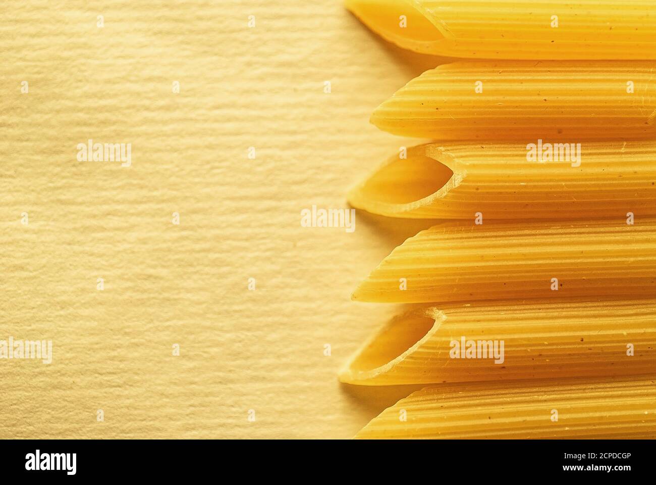 Border of dried Italian penne pasta tubes over a textured yellow background with copyspace Stock Photo
