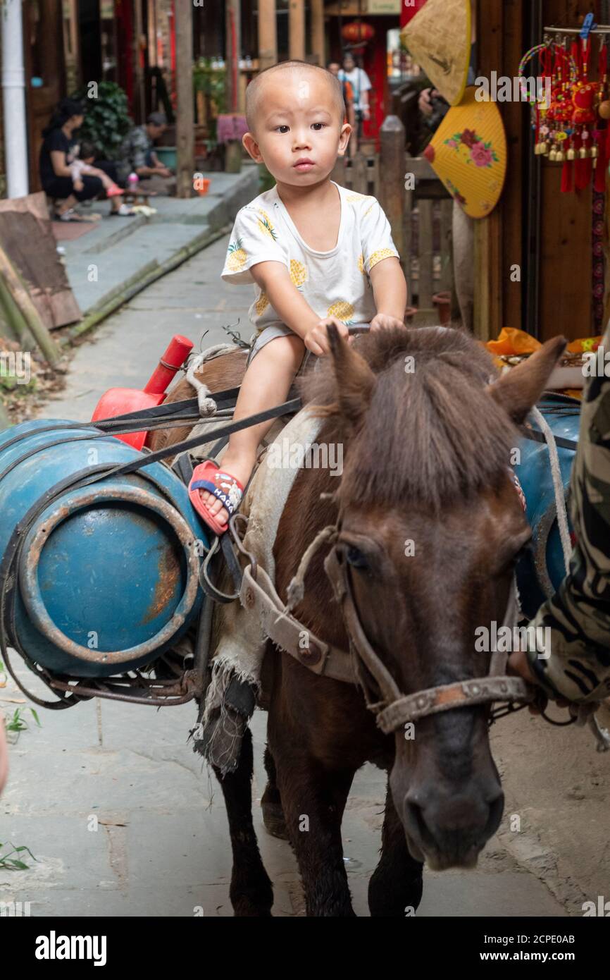 A boy rides on a horse in the narrow streets of Ping'an. Stock Photo