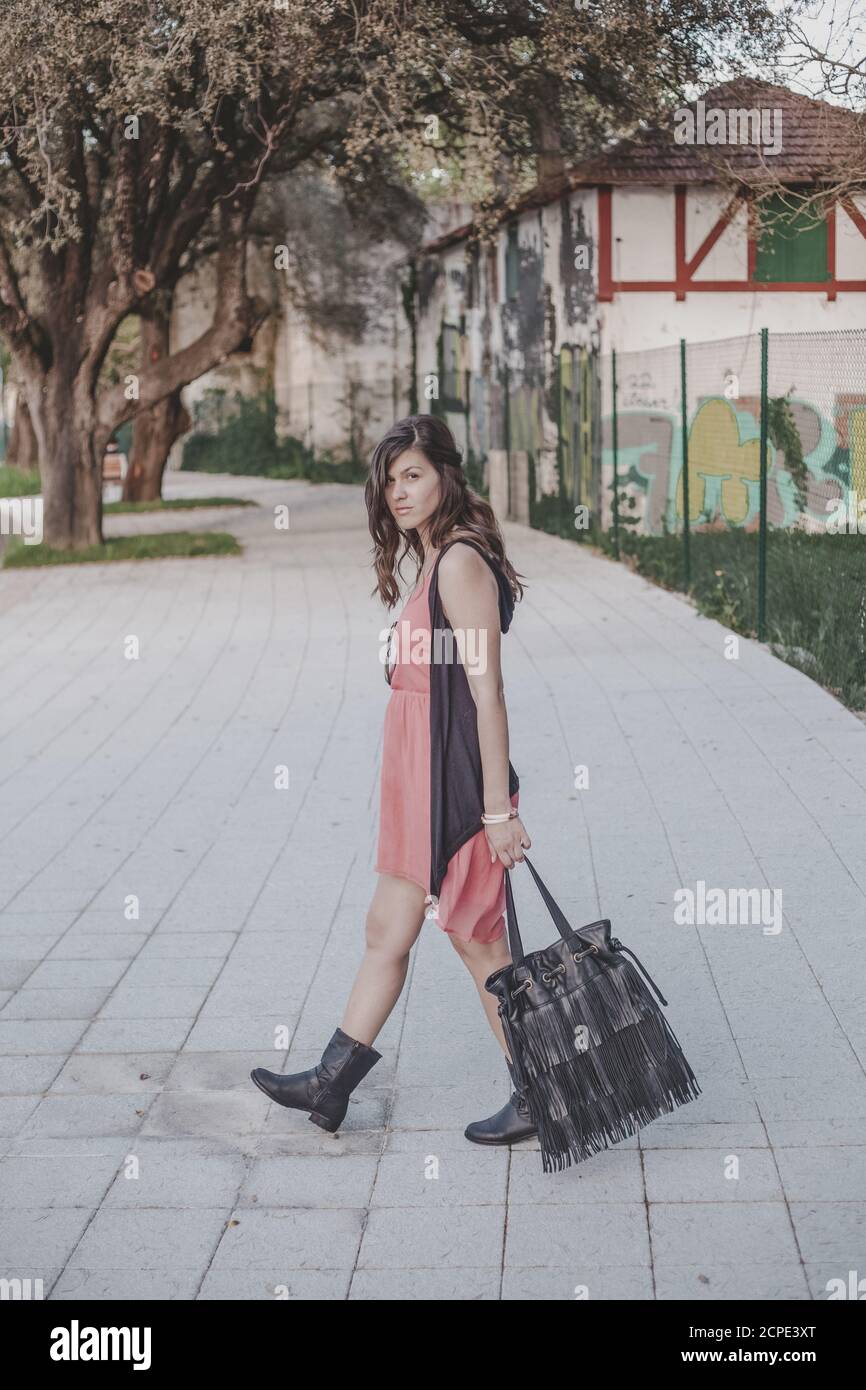 Young beautiful Latin female wearing a coral dress, boots and holding a