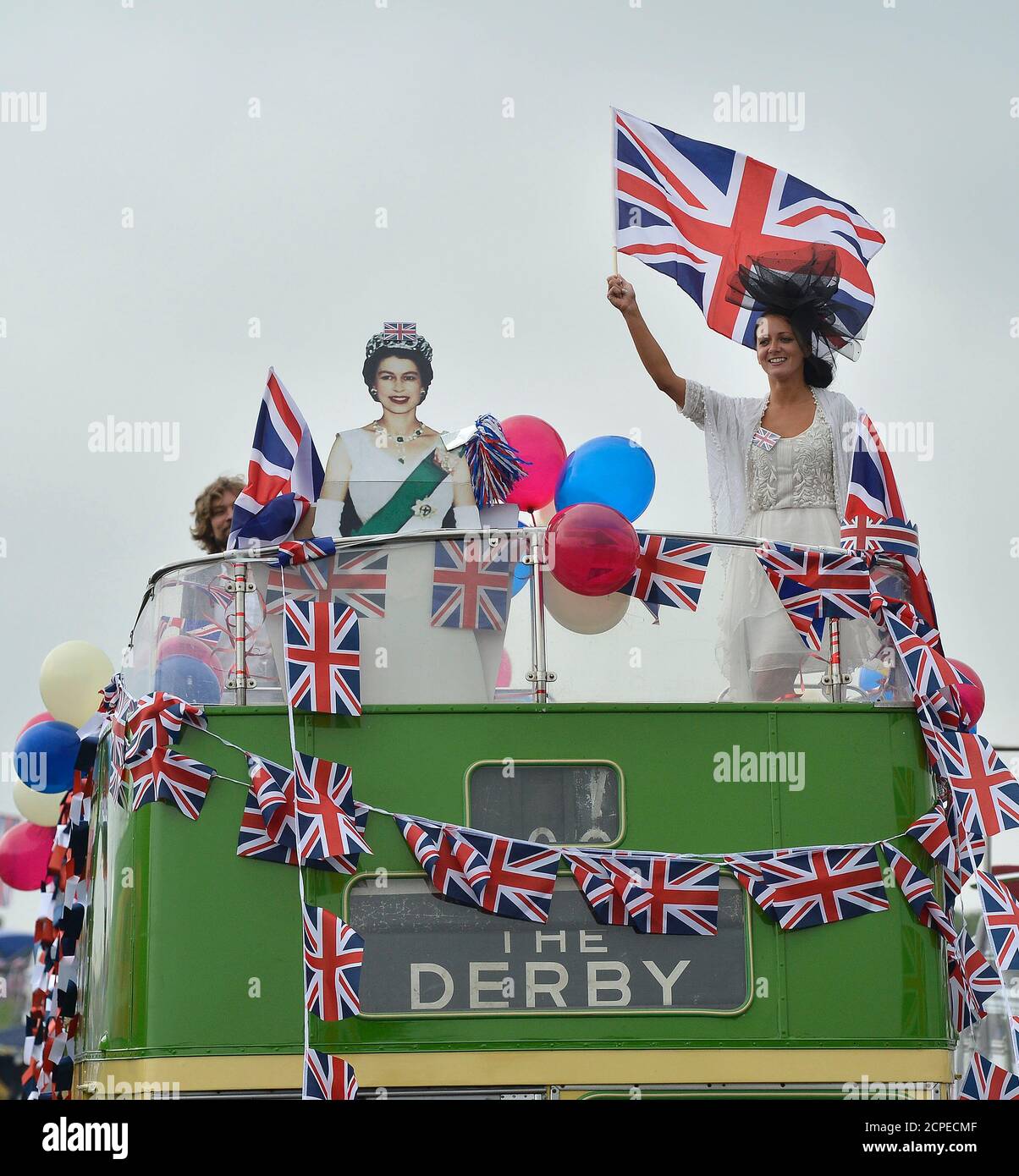 A racegoer waves a Union Jack flag next to a cardboard cut-out of Queen  Elizabeth on an open-top bus at the Epsom Derby festival in Epsom,  southwest of London June 2, 2012.