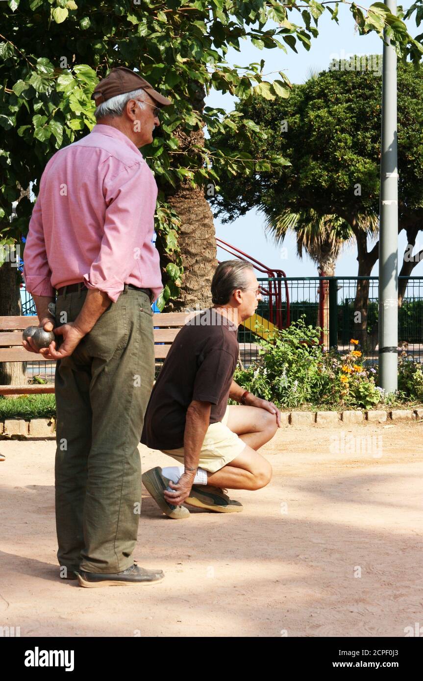 Petanque game on the beach promenade. Serious, prestigious pensioners. Focus on small yellow balls. Focus before the throw. Stock Photo