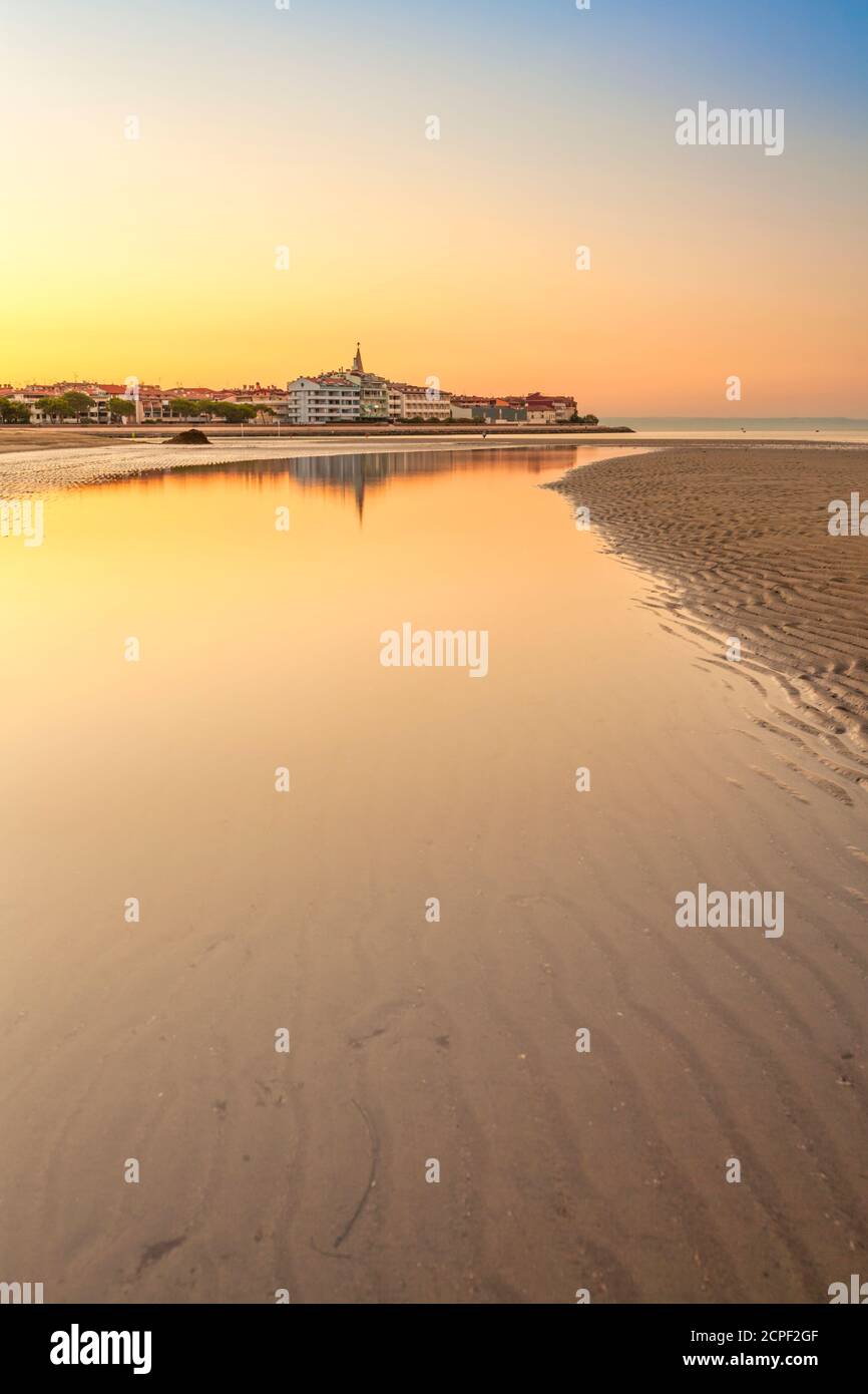 Colorful orange beach at sunset with ripple sand patterns from the receding tide and reflections on the water of the lagoon in a tranquil scenic lands Stock Photo