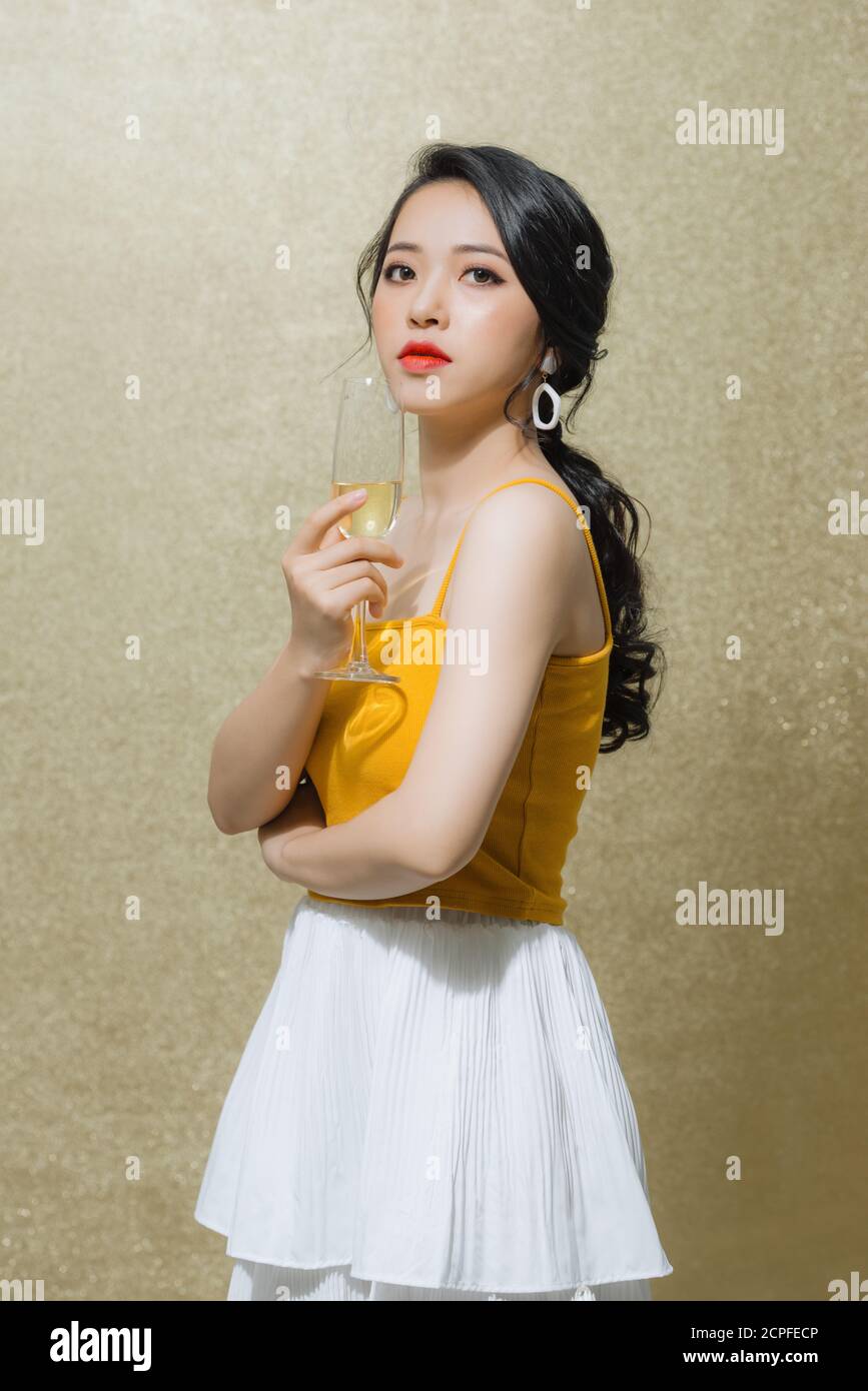 Portrait of beautiful young Asian woman holding wine glass over gold ...