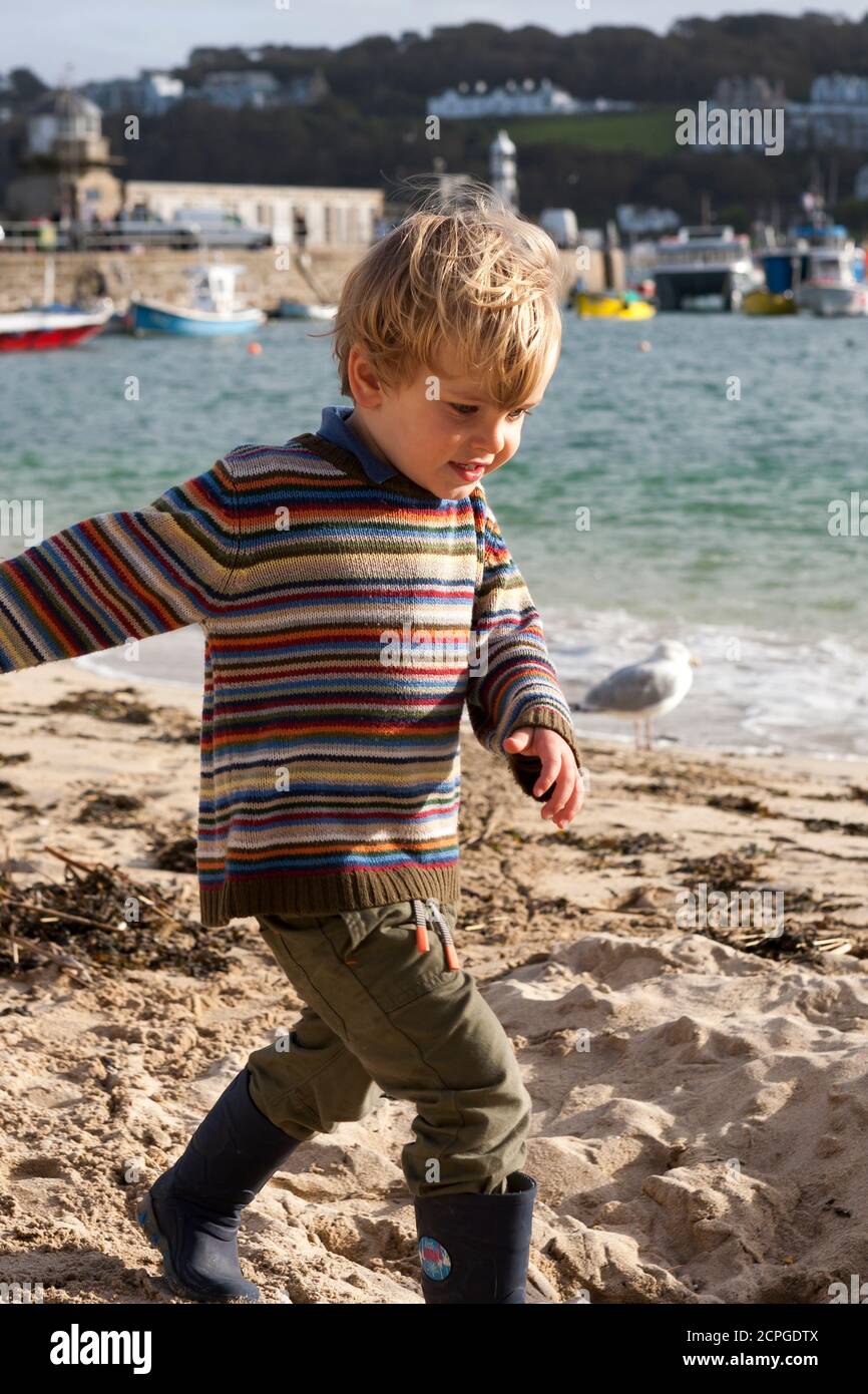 Little boy (2/3 years old), wearing pullover and wellingtons, playing on the sand on a chilly afternoon: St. Ives, Cornwall, UK.  MODEL RELEASED Stock Photo