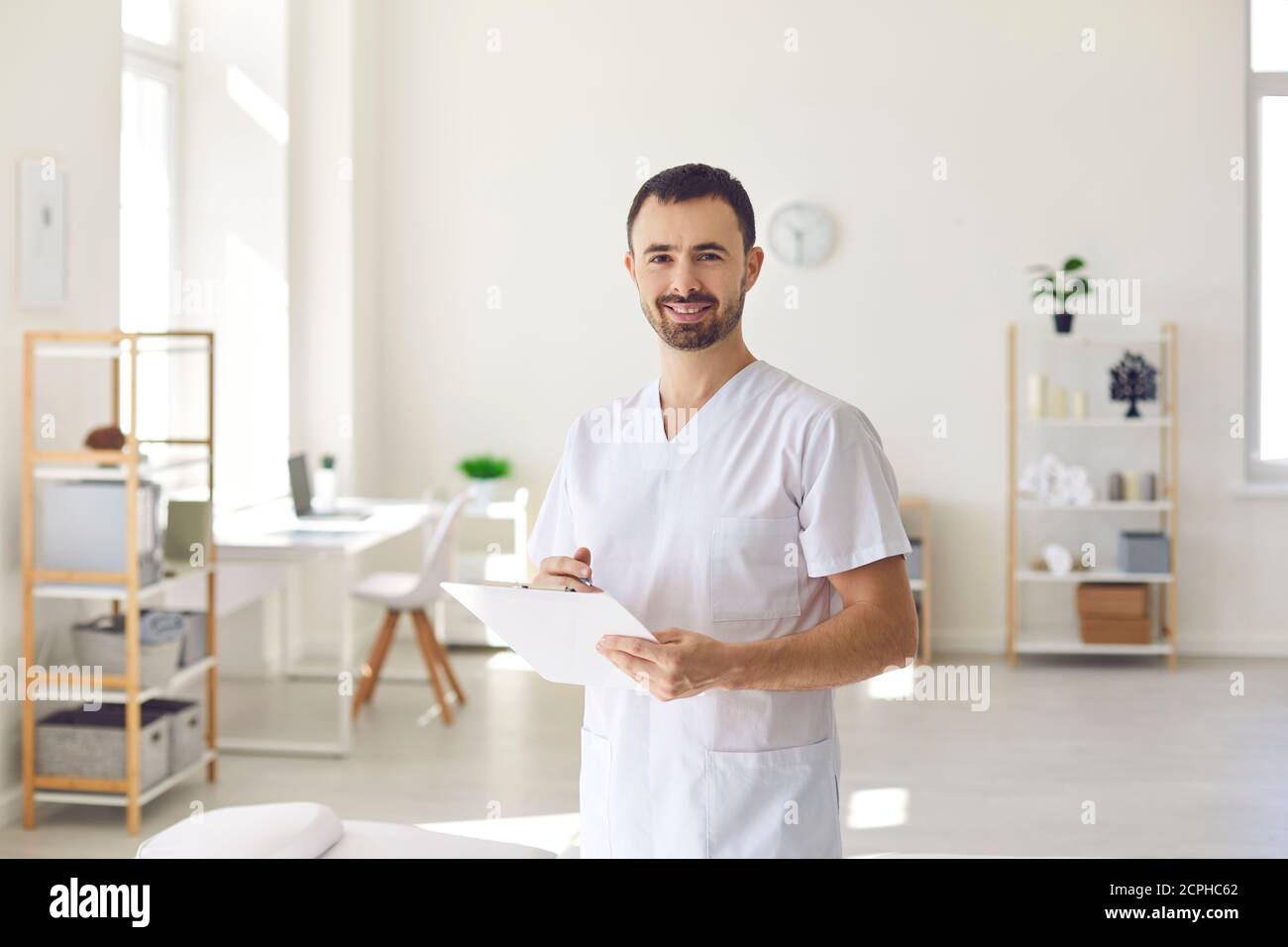 Smiling man doctor chiropractor or osteopath standing with notes and looking at camera Stock Photo