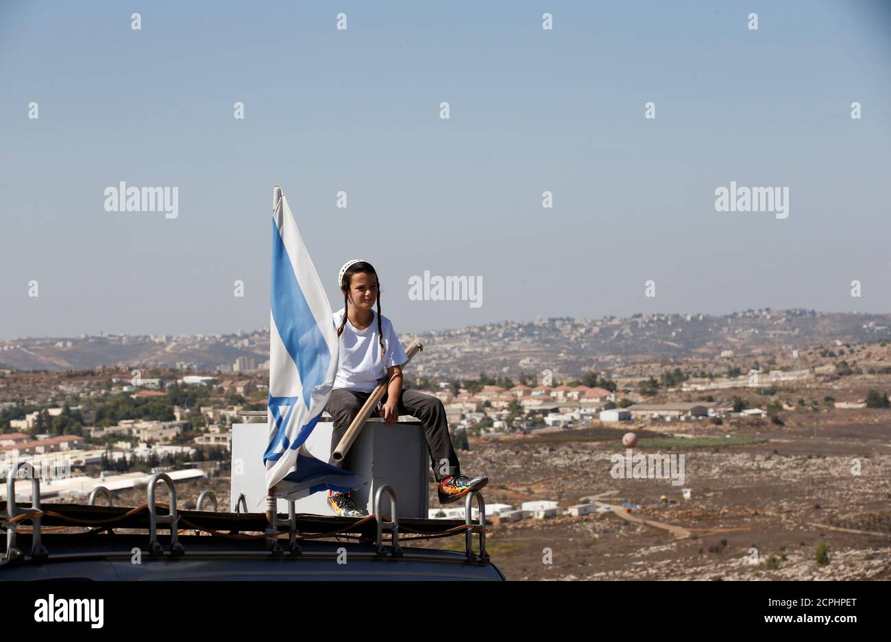 A boy sits near an israeli flag atop the roof of a vehicle at the entrance to the Jewish settler outpost of Amona in the West Bank, during an event organised to show support for Amona which was built without Israeli state authorisation and which Israel's high court ruled must be evacuated and demolished by the end of the year as it is built on privately-owned Palestinian land, October 20, 2016. REUTERS/Ronen Zvulun Stock Photo