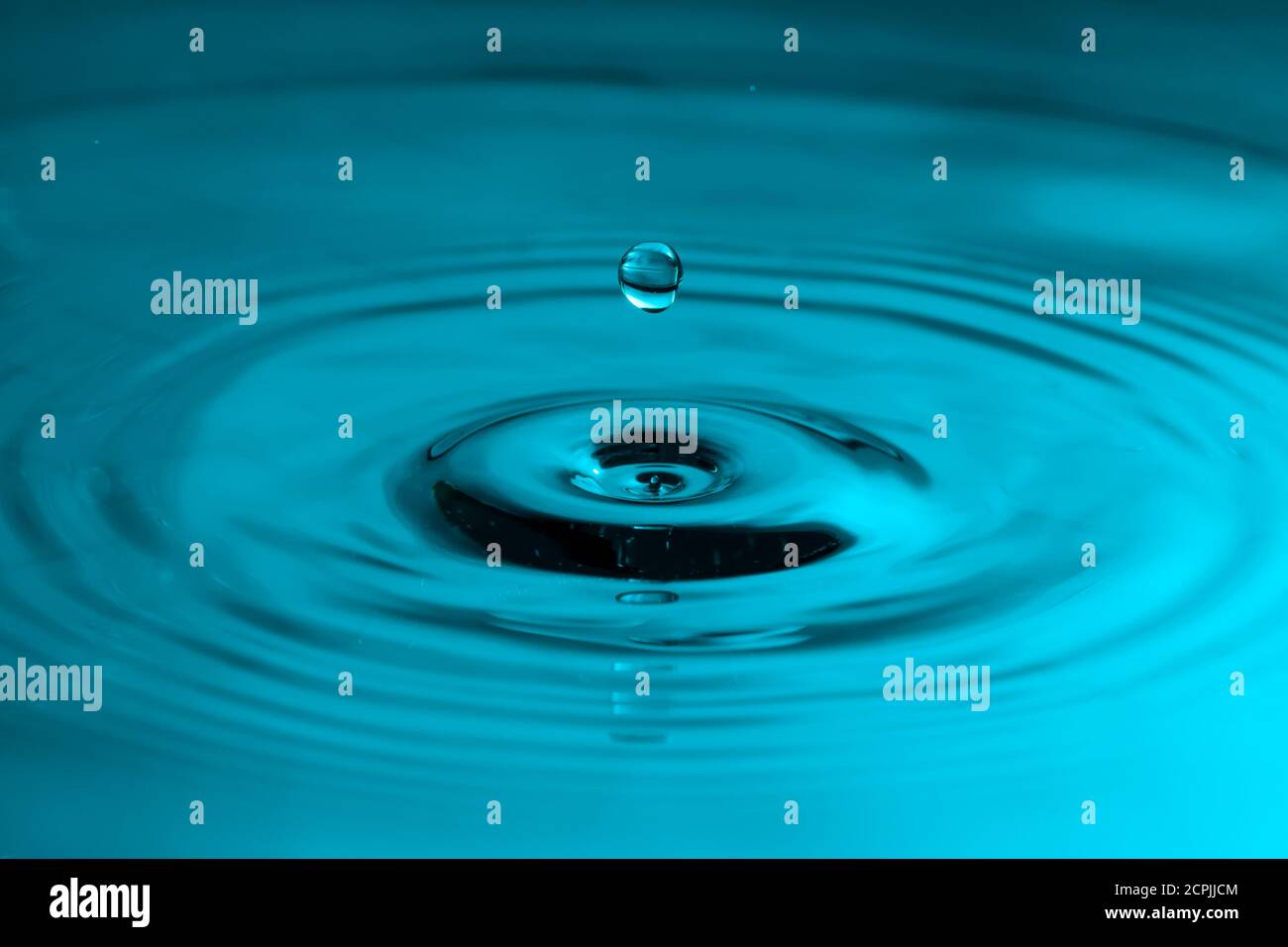 Perfect water drop splashing into smooth water causing ripples Stock Photo