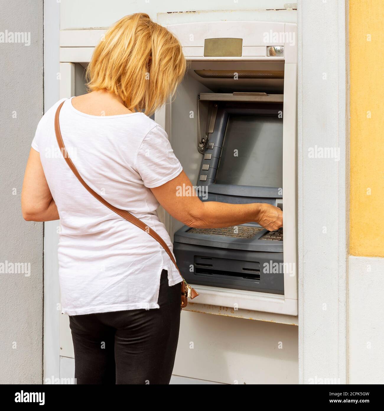 Blond white woman withdraws cash from an ATM Stock Photo