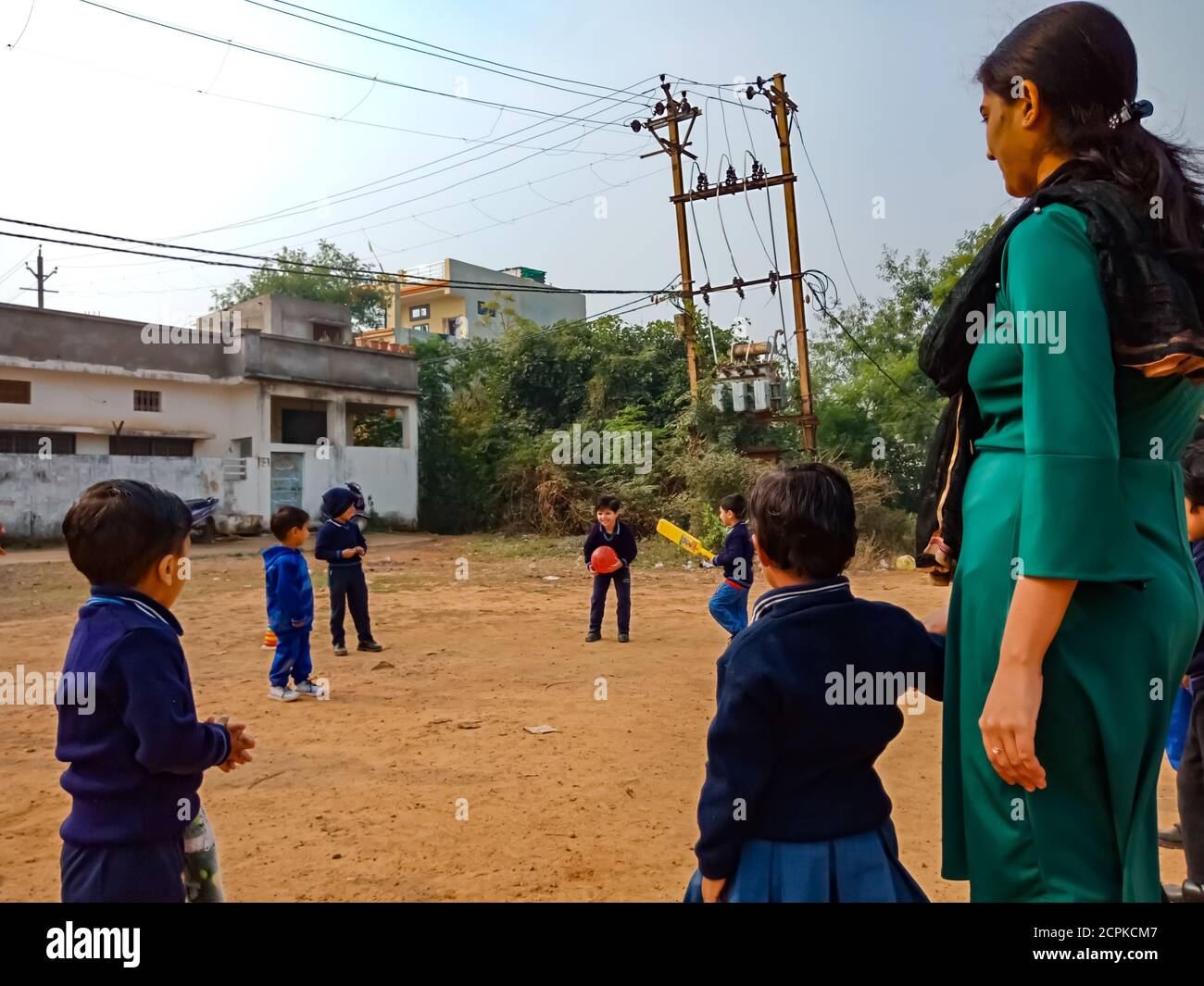 DISTRICT KATNI, INDIA - JANUARY 17, 2020: Indian preschool kids playing game together with lady teacher at soil field on sport ground. Stock Photo