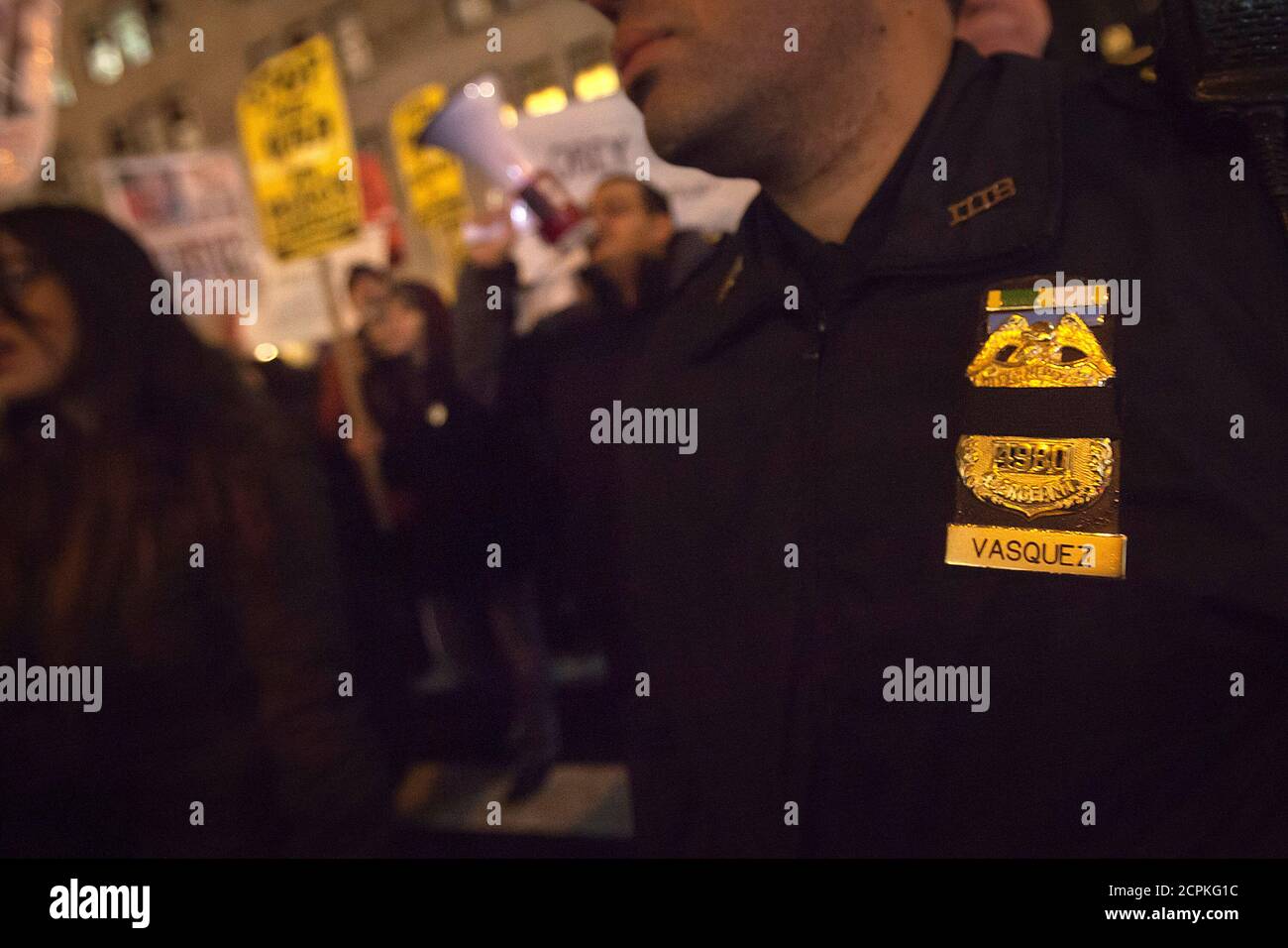 A policeman wearing a mourning band on his badge monitors a protest against the police in the Manhattan borough of New York December 23, 2014.Mayor Bill de Blasio's attempts to soothe a city dismayed by the slaying of two officers were further rebuffed on Tuesday as protesters defied his call to suspend what have become regular demonstrations over excessive police force. REUTERS/Carlo Allegri (UNITED STATES - Tags: CRIME LAW CIVIL UNREST) Stock Photo