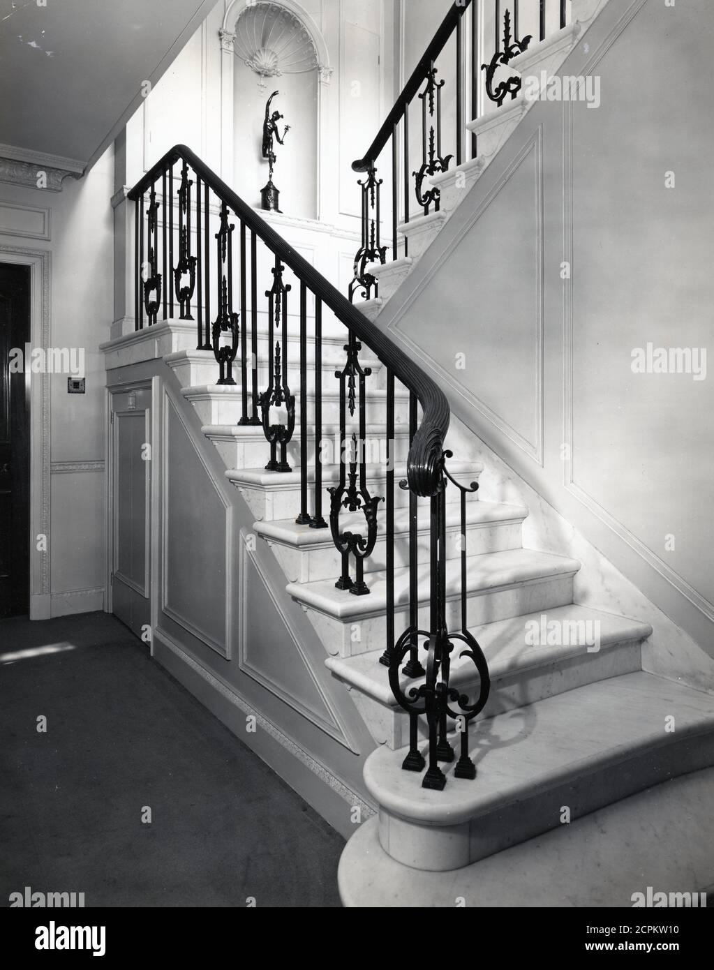 An architectural staircase to quarter landing with contemporary cast iron decorated balusters. Possibly 1930s. Taken from an original photograph by D Griffin for the London photographers Larkin Brothers Stock Photo