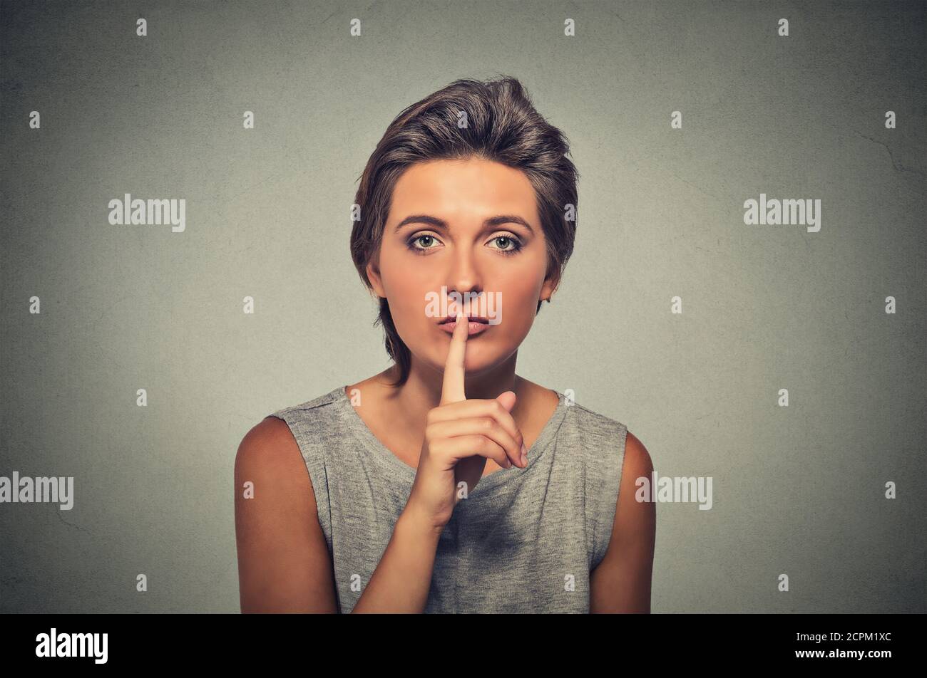 Closeup portrait of secret woman. Young female showing hand silence sign, asking someone to keep it quiet, isolated on gray background. Human communic Stock Photo