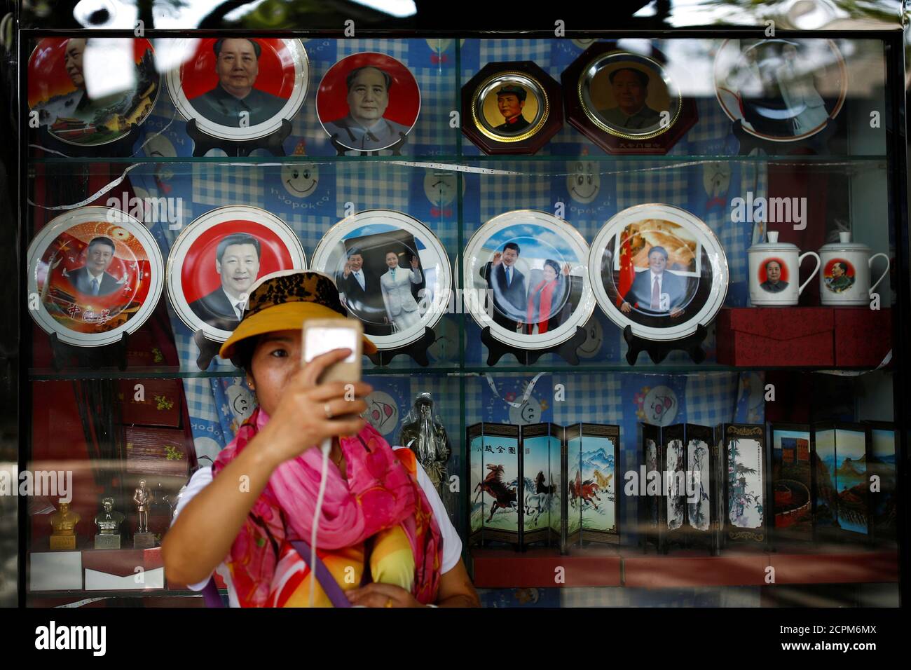 A woman takes a selfie in front of souvenirs featuring portraits of China's late Chairman Mao Zedong and China's President Xi Jinping outside a shop near the Forbidden City in Beijing, China, September 9, 2016. REUTERS/Thomas Peter Stock Photo