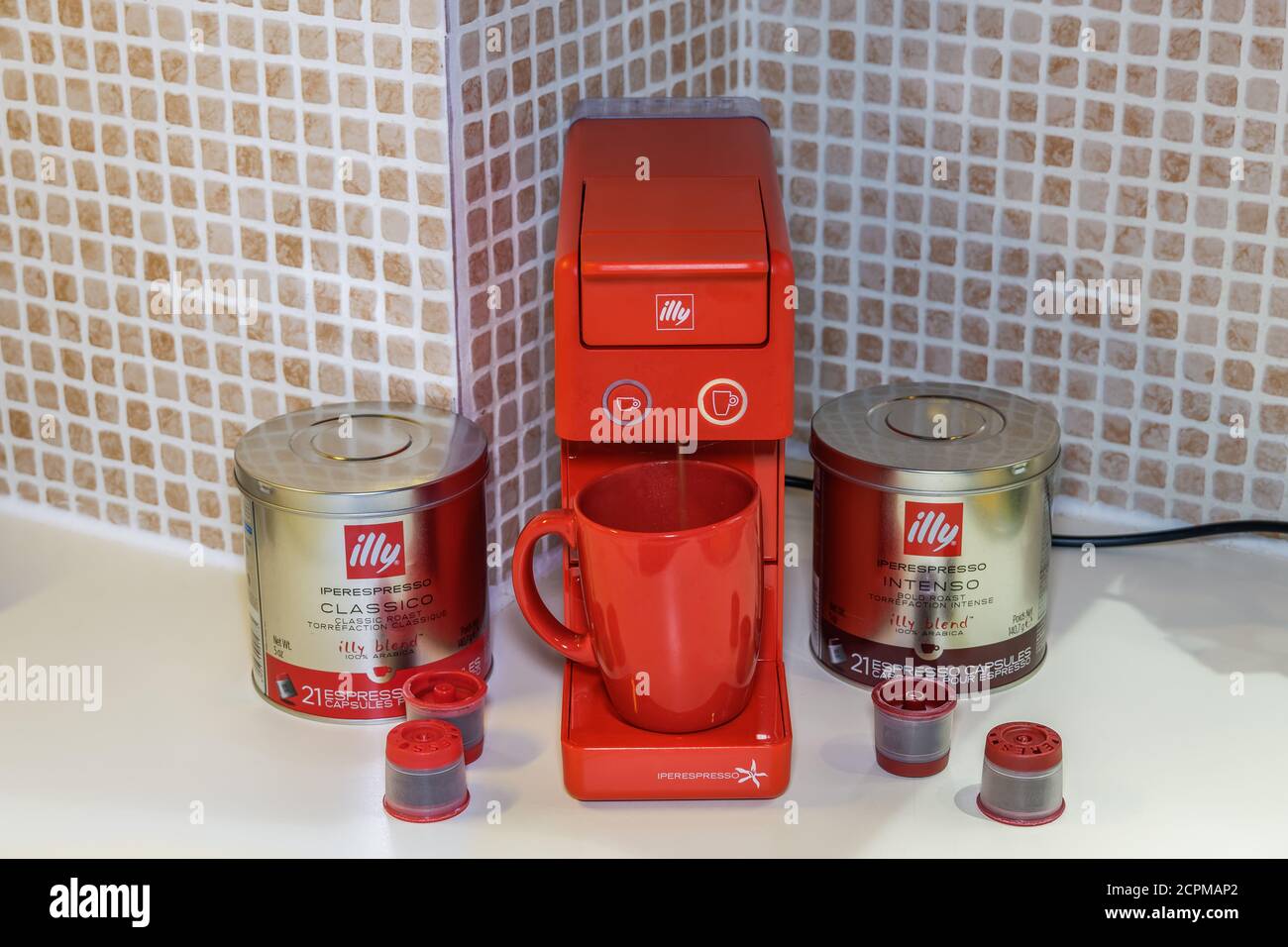 Automatic Illy iperespresso machine to create espresso with single-serve capsules. Pods with case and Illy logo around red electric coffeemaker. Stock Photo