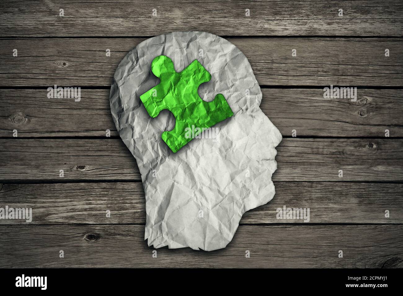 Puzzle head solution concept as a human face profile made from crumpled white paper with a jigsaw piece cut out inside the brain area on old wood back Stock Photo