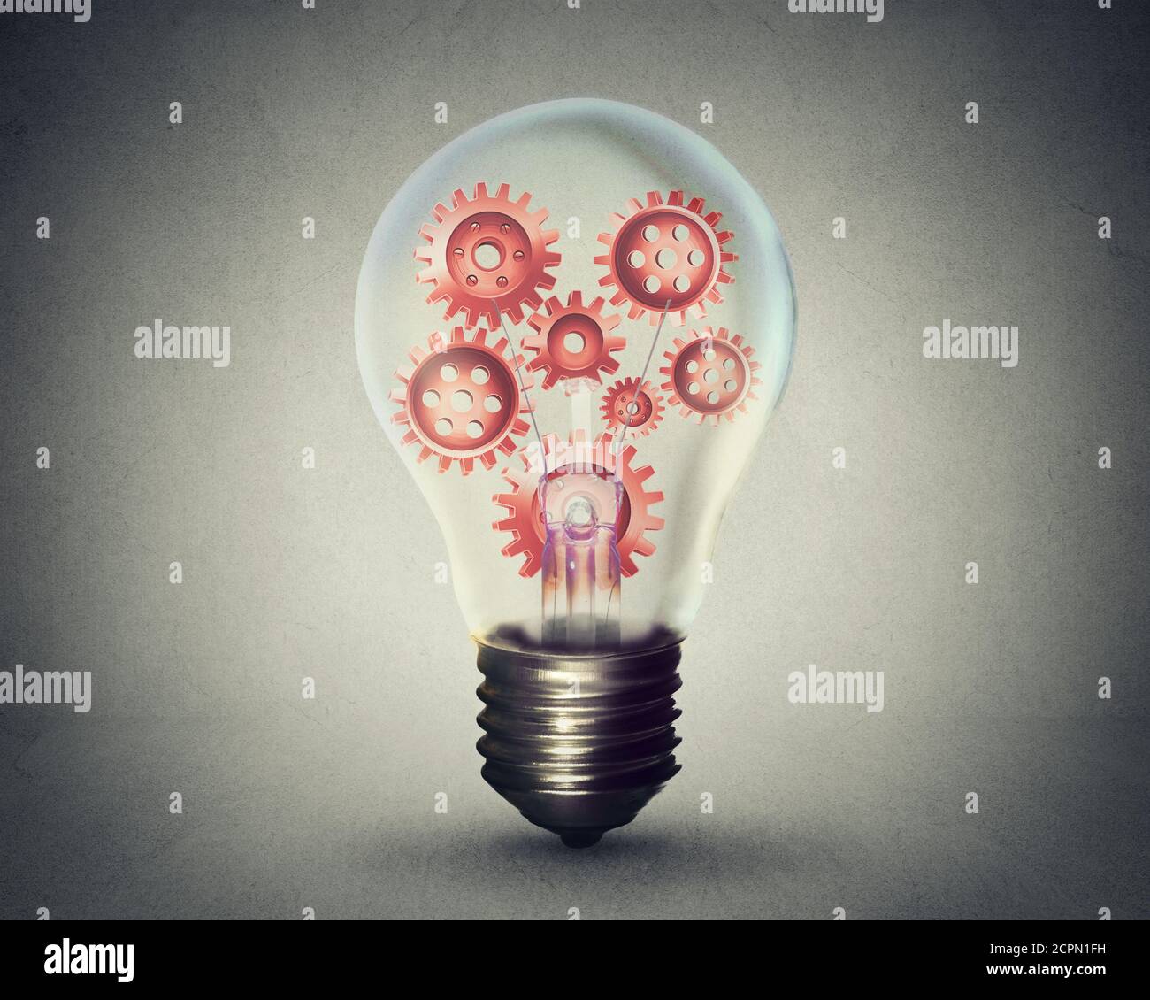 light bulb with gears and cogs working together isolated on gray wall background Stock Photo