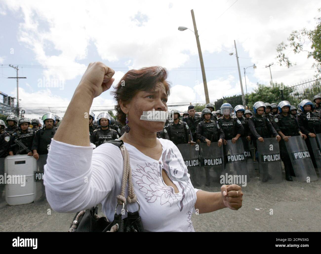 A supporter of Honduras' ousted President Manuel Zelaya shouts next to riot police with her mouth taped during a protest in Tegucigalpa September 28, 2009. Honduras' de facto government on Monday resisted pressure from opponents and the international community over ousted President Manuel Zelaya, who for a week has been holed up inside the Brazilian embassy seeking a return to power.  REUTERS/Henry Romero (HONDURAS MILITARY POLITICS CONFLICT) Stock Photo
