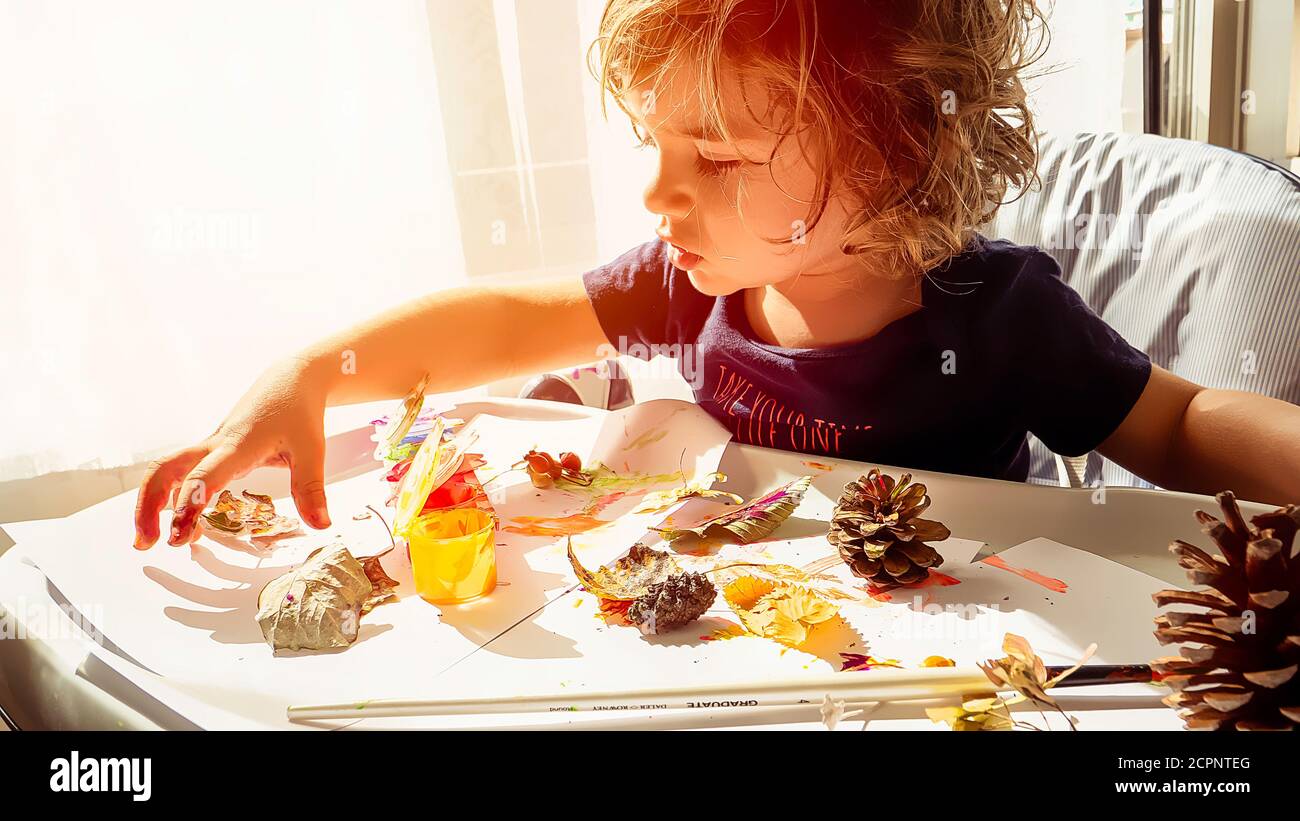 Toddler boy is home schooled painting yellow leaves and pine cones in