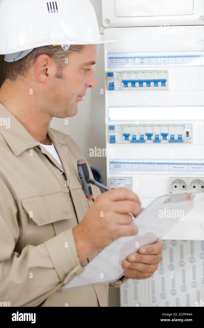 male technician holding clipboard while examining fusebox Stock Photo