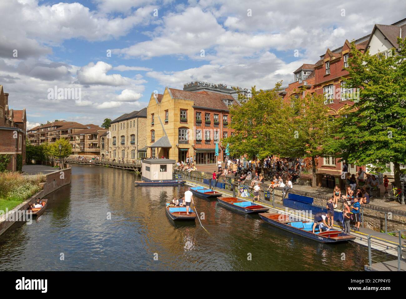 People enjoying a summer afternoon beside punts on the River Cam viewed from Magdalene Bridge, Cambridge, UK. Stock Photo