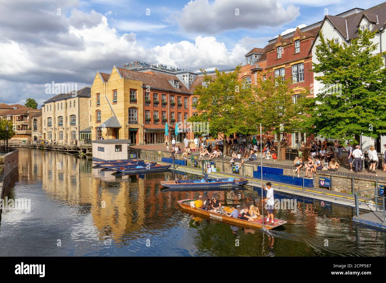 People enjoying a summer afternoon beside punts on the River Cam viewed from Magdalene Bridge, Cambridge, UK. Stock Photo